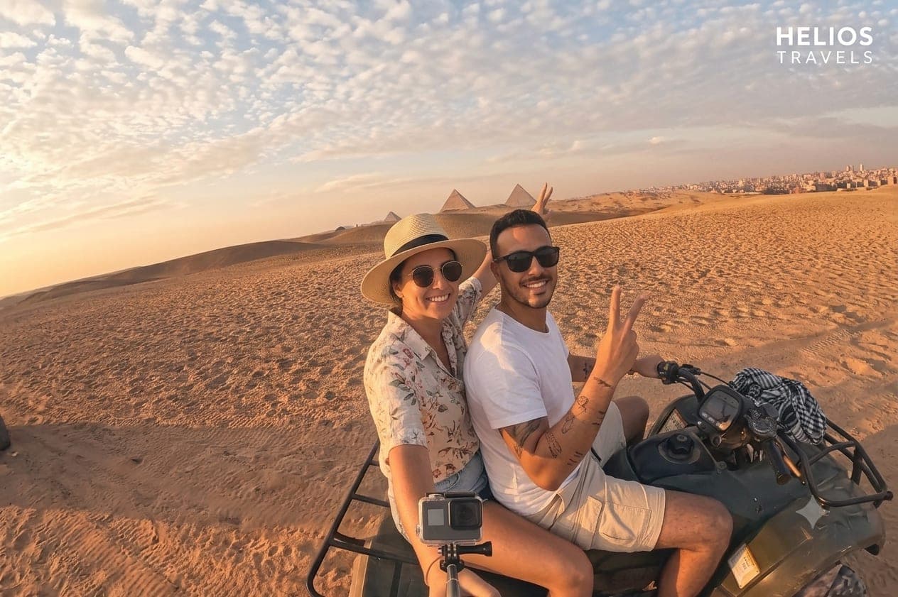 Tourists taking a selfie with the Giza Pyramids while riding a quad bike through the desert.