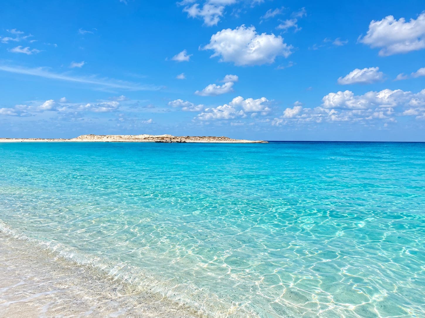 Crystal-clear Mediterranean water meeting a white sandy beach under a bright blue sky on Egypt’s North Coast.